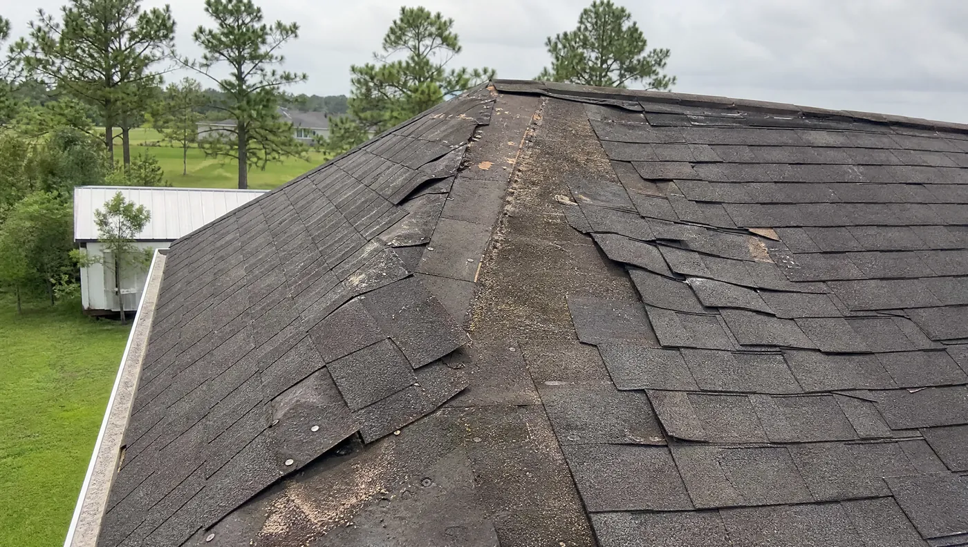 Storm damaged shingle roof with creased tabs and exposed decking in Rosharon TX